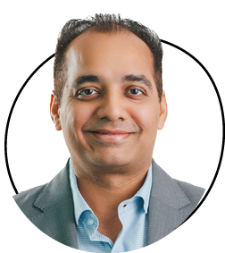 Man smiling in a suit and light blue shirt, facing forward.