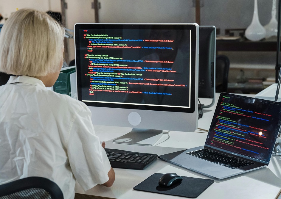 A woman doing coding on a desktop computer and on a laptop