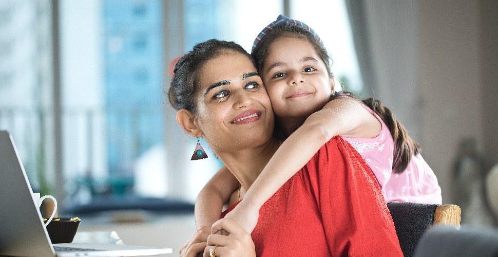 One woman holding her daughter while sitting at her work desk with a laptop