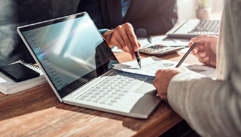 Two people reviewing financial documents at a wooden desk with a laptop and calculator, suggesting a professional compensation discussion or negotiation meeting.