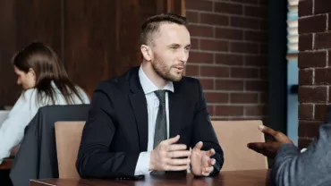 Two people in formal attire having a conversation at a table.