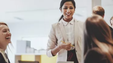 Group of people having a meeting in an office, one person standing and speaking.