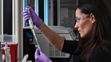 Person in lab coat using a pipette with samples nearby in a laboratory.