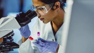 Scientist examining samples through a microscope in a lab.