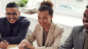 Three people smiling during a meeting at a table.