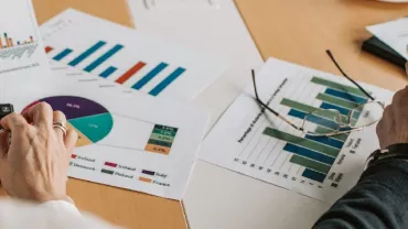 People reviewing charts and graphs at a desk with a calculator.