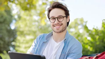 Person sitting outdoors smiling with a tablet.