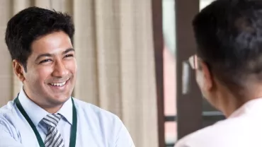 A man in a work outfit smiling to another person