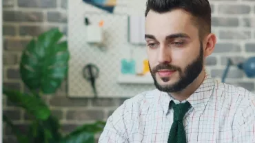 Person in an office setting with a brick wall and plants in the background.