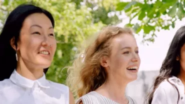 Three people walking outdoors, smiling under a tree.