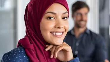 Person smiling in a professional setting with colleagues in the background.