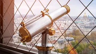 Telescope on a platform overlooking a cityscape with a grid fence.