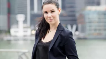 Person in a blazer standing in front of a cityscape with skyscrapers.