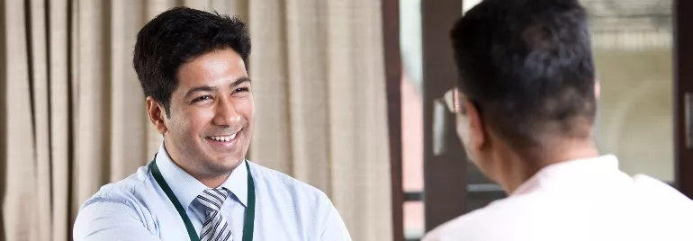 A man in a work outfit smiling to another person