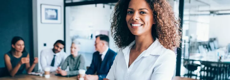 Smiling person standing in a modern office with colleagues in the background.