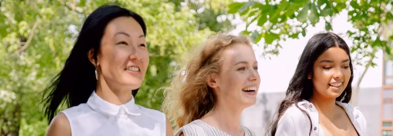 Three people walking outdoors, smiling under a tree.